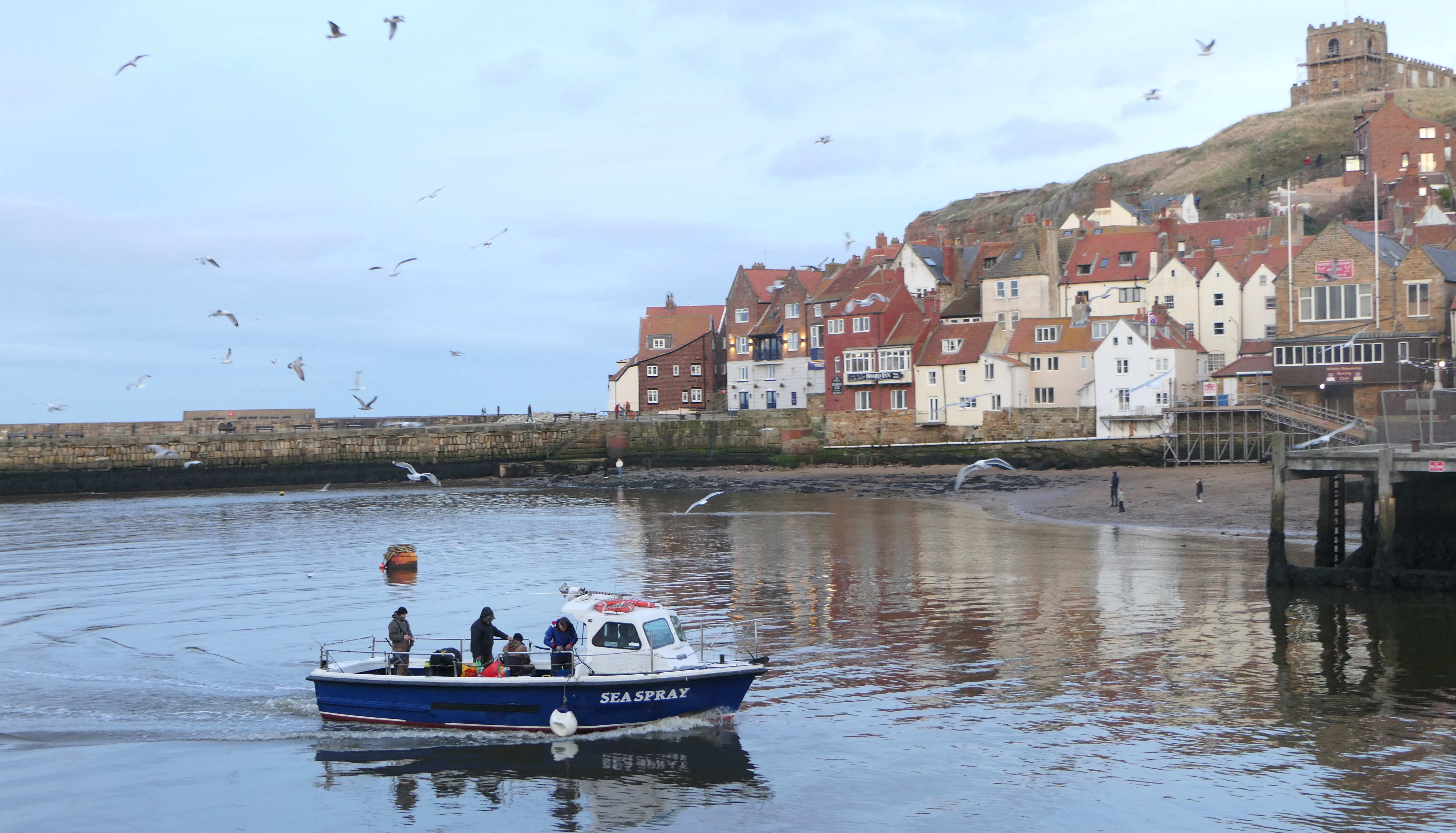 The Seaspray boat is returning to the harbour with the famous abbey at Whitby in the background